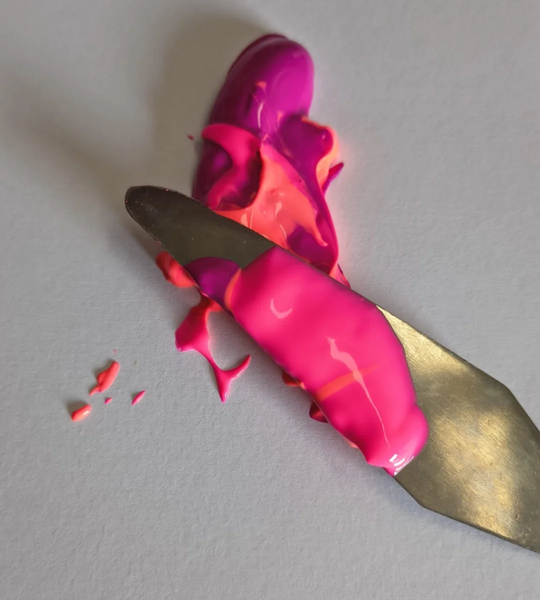 Spachtel mit leuchtend pinker Farbe auf einer hellen Malunterlage.